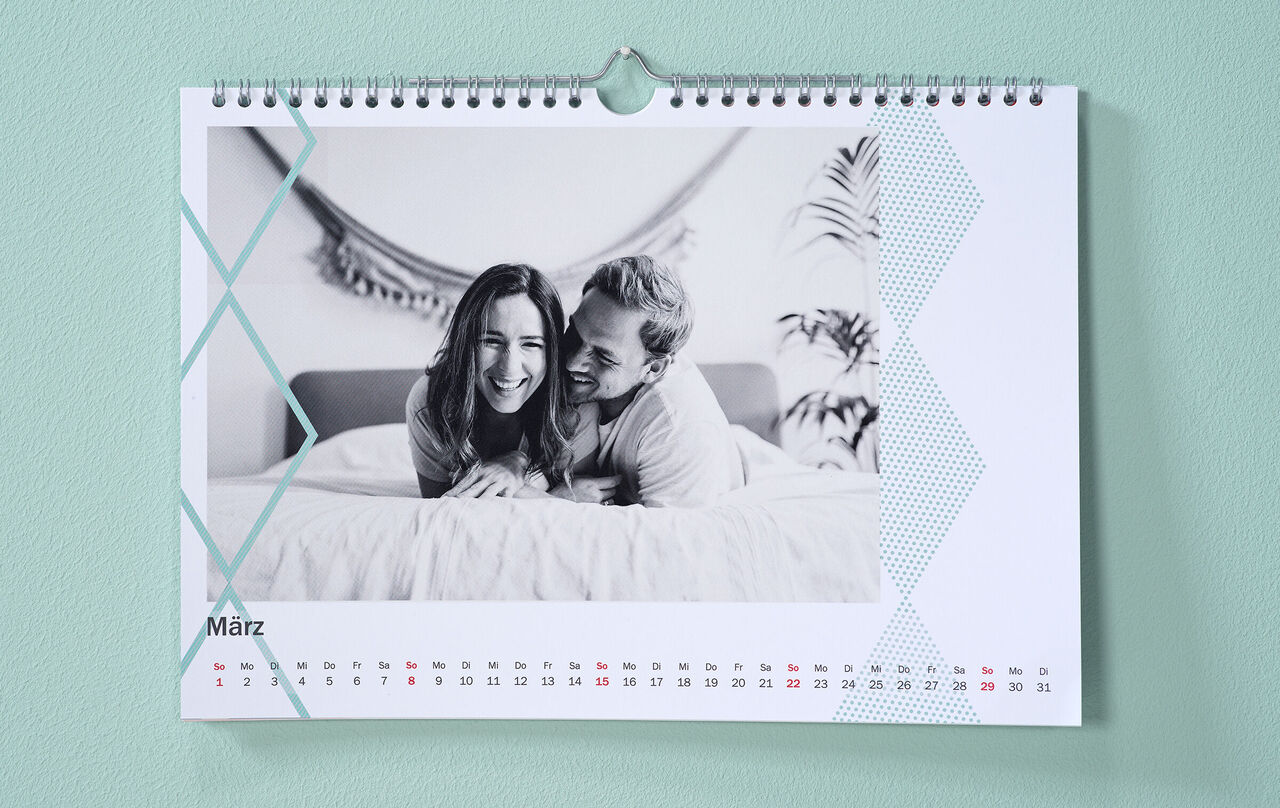 Egy egyedi naptár a szerelmespár fotójával és zöld színű szegélyes cliparttal lóg a falon.