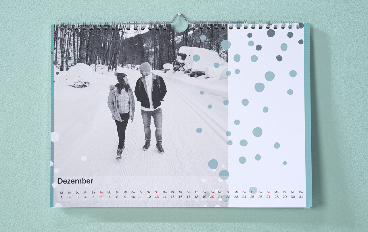 Egy télies hangulatú naptár a szerelmespár fotójával és pöttyös cliparttal a falon lóg.