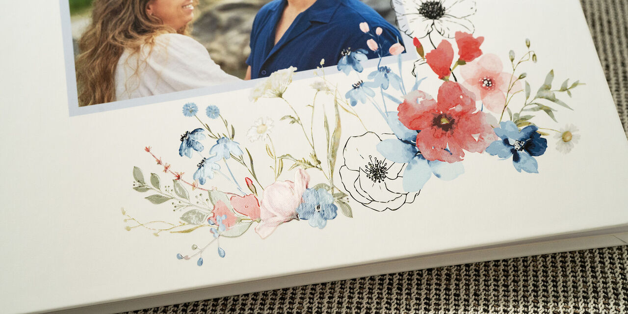 Közeli kép a vendégkönyv borítójáról, az ifjú pár fényképével. A könyvet virágos esküvői dizájn és fehér alapon effektlakkozás teszi elegánssá.